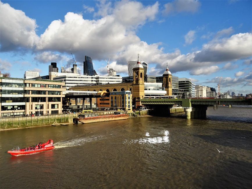 A view of multiple dark metal pedestrian bridges connecting two rows of brick buildings with large, arched windows in Bermondsey, London. The bridges have decorative railings and supporting brackets,