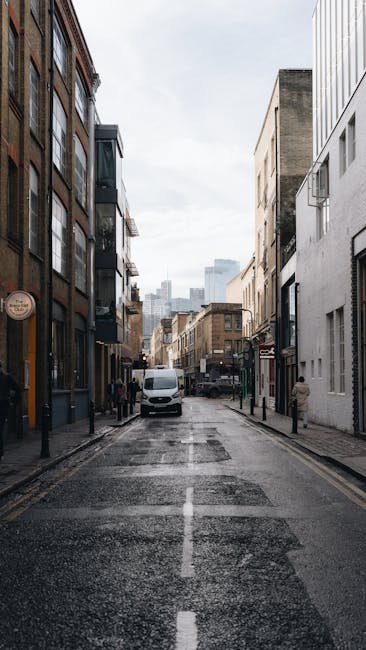 A narrow urban street scene viewed from the perspective of a house moving operation near Tower Bridge Road, with modern and older commercial buildings on both sides. In the foreground, the street has 